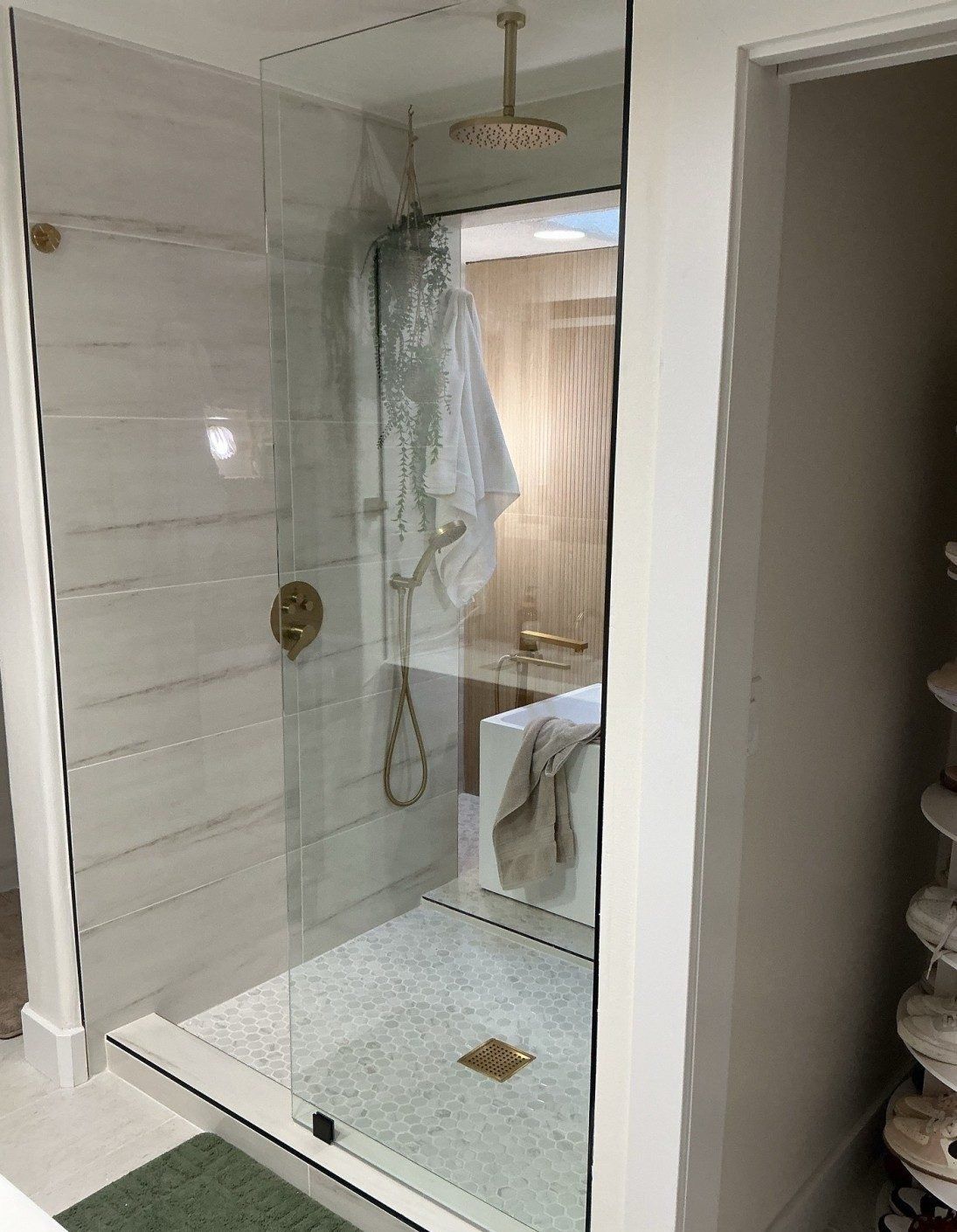 Frameless fixed glass shower panel with brushed gold clamps and rain shower head in a Phoenix area home