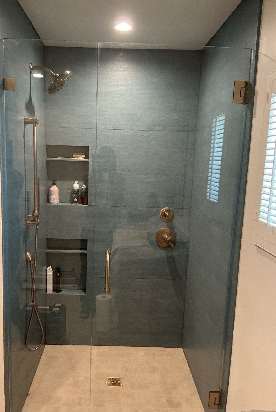 Frameless glass shower enclosure with teal tile niche and brushed brass fixtures in a Phoenix area bathroom