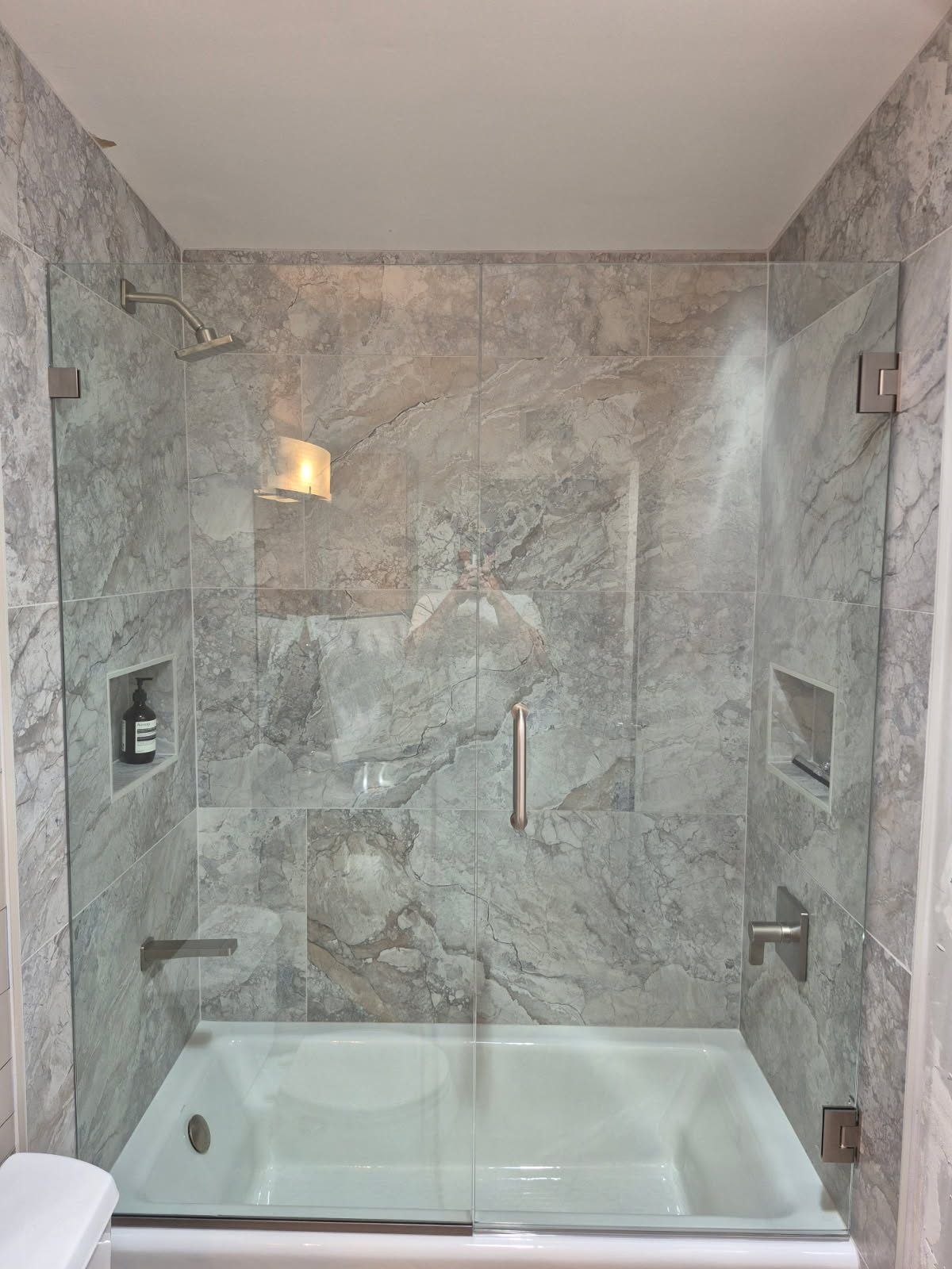 Frameless glass tub enclosure with hinged door and fixed panel over a soaking tub with gray marble tile in Phoenix AZ