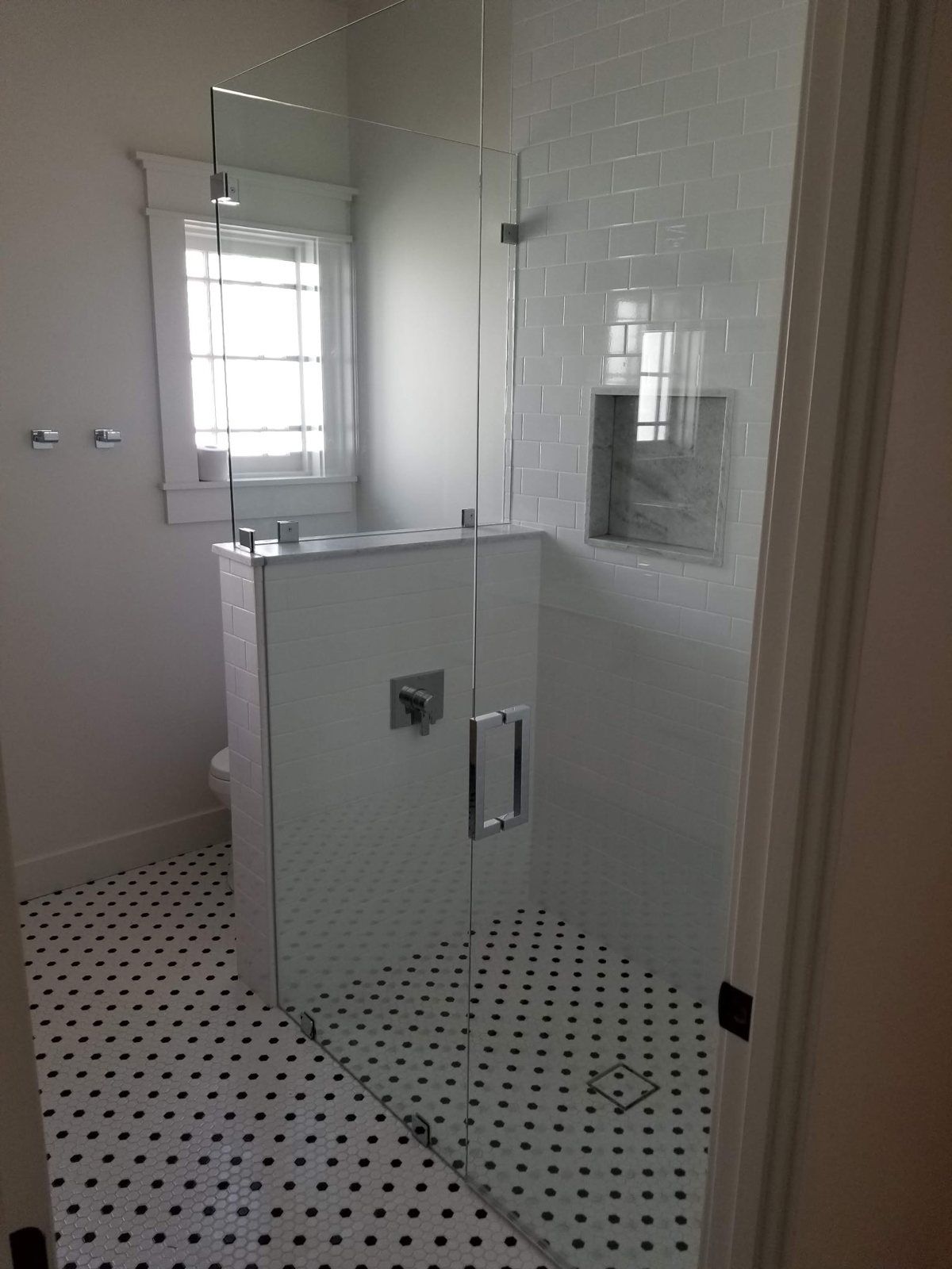 Frameless glass shower enclosure on a tiled knee wall with chrome handle and hex tile floor in a Phoenix bathroom