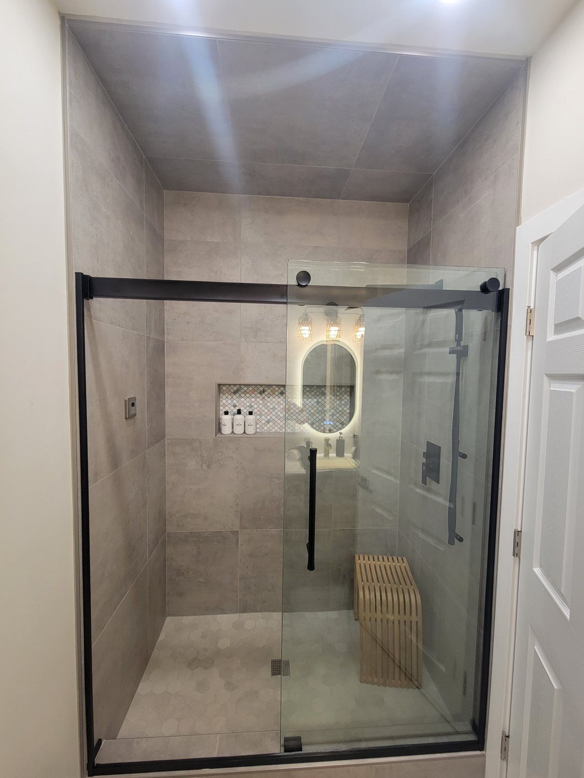 Frameless sliding shower door with matte black roller bar, handle and bench in a Phoenix bathroom