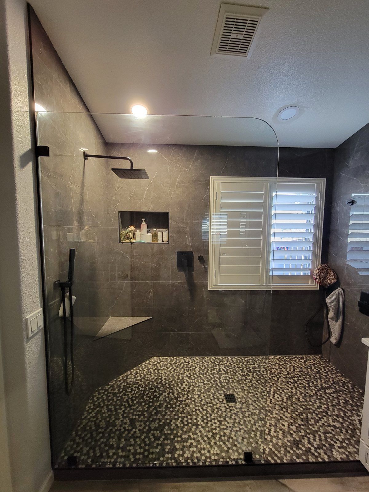 Frameless walk-in shower glass panel with matte black hardware and pebble floor in a Phoenix bathroom