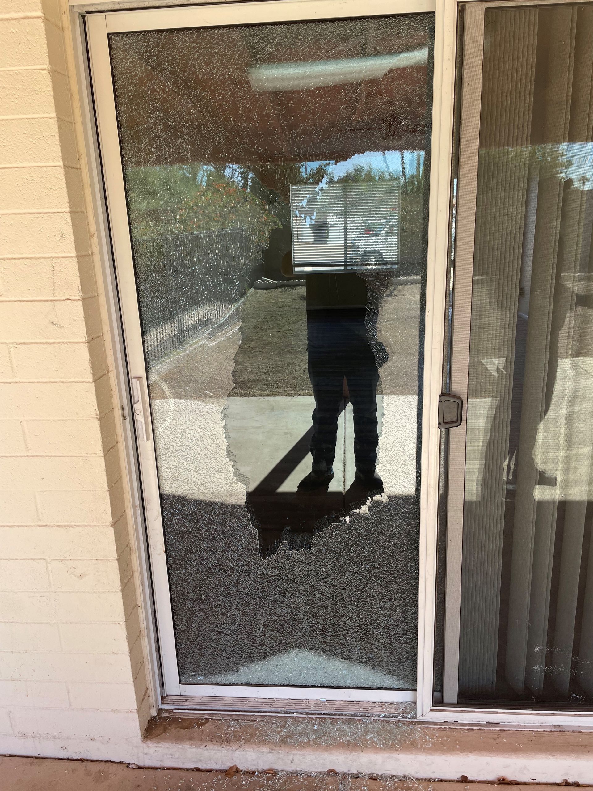 Shattered sliding glass door; person stands nearby, visible reflection; building exterior.