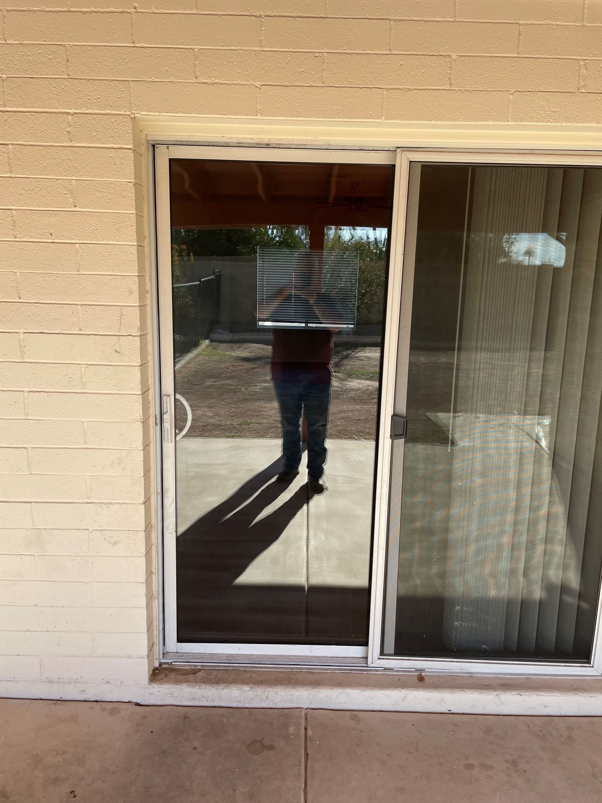 Person reflected in sliding glass door, standing outside on concrete patio; sunlit.