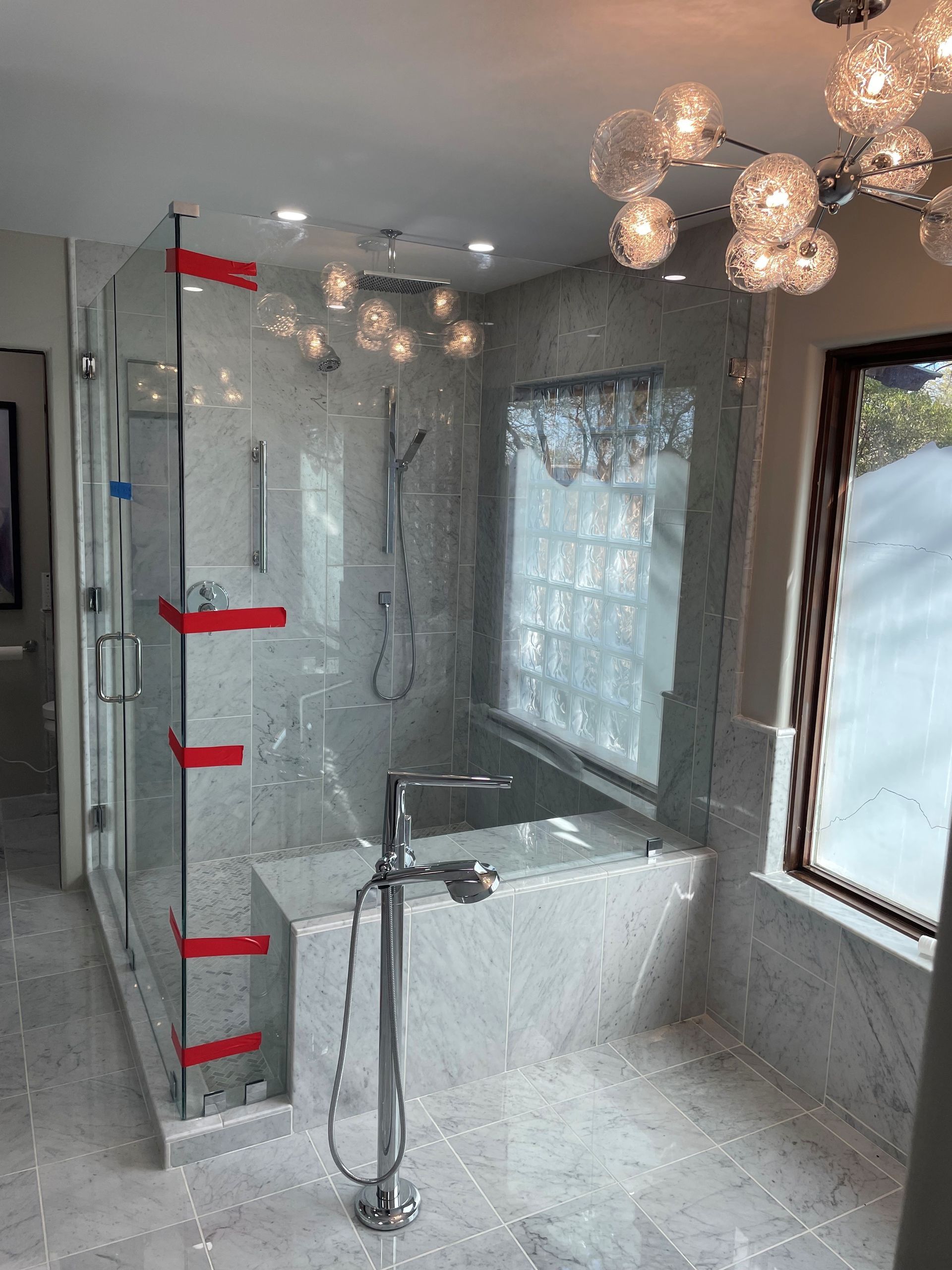 Modern bathroom with glass shower, gray tile, and a window.
