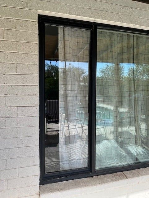 Black-framed sliding glass door on a white brick wall, reflecting outdoor patio furniture and pool.