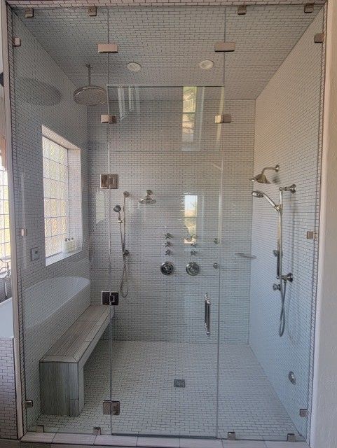 Spacious glass shower with multiple showerheads, a built-in bench, and white tiled walls.