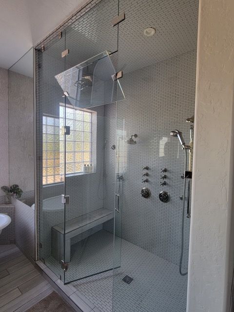 Modern shower with glass enclosure, tiled walls, bench, and multiple showerheads.