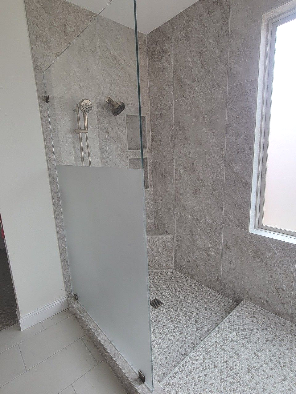 Modern tiled walk-in shower with glass partition and chrome fixtures beside a window.