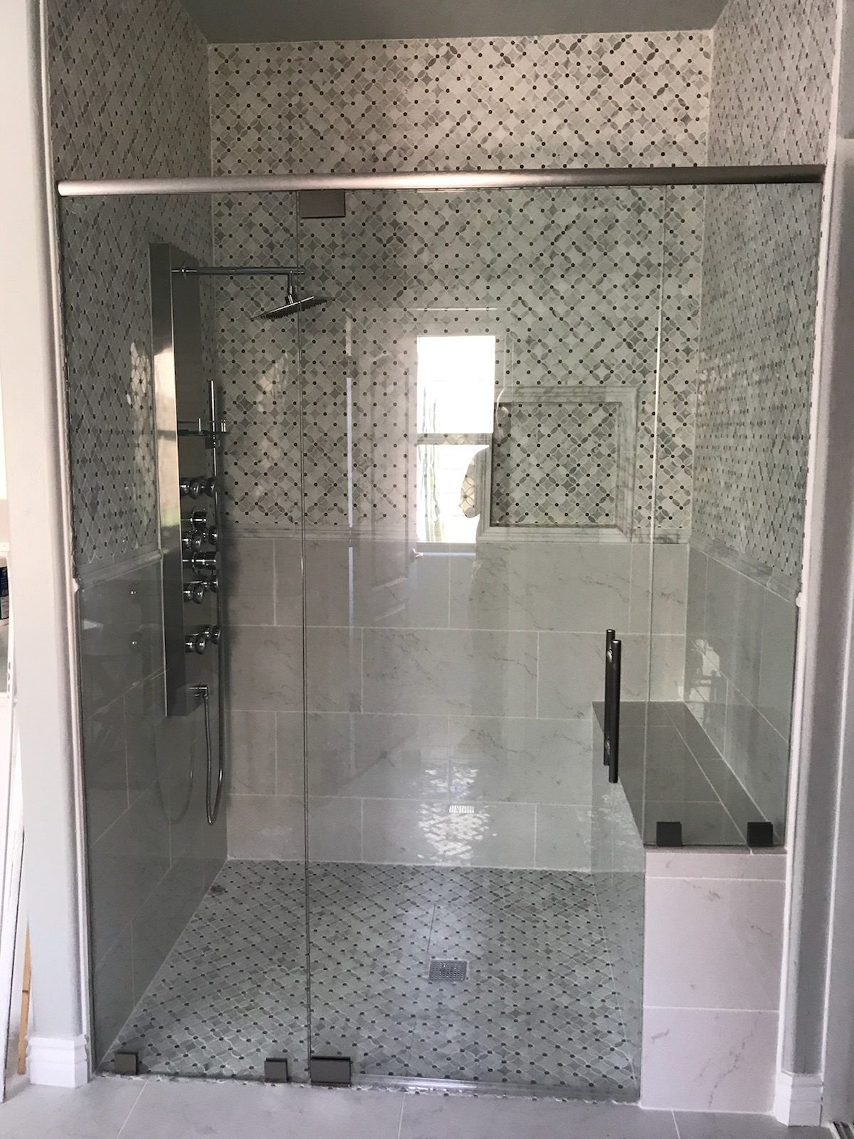 Wide glass shower enclosure with sliding panel and support bar over patterned tile and bench in a Phoenix area home