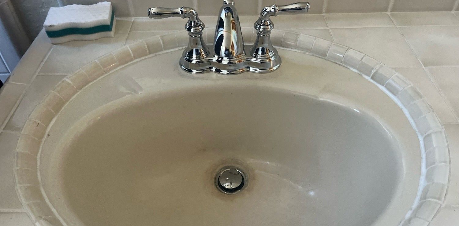 White oval bathroom sink with chrome faucet and beige countertop tiles
