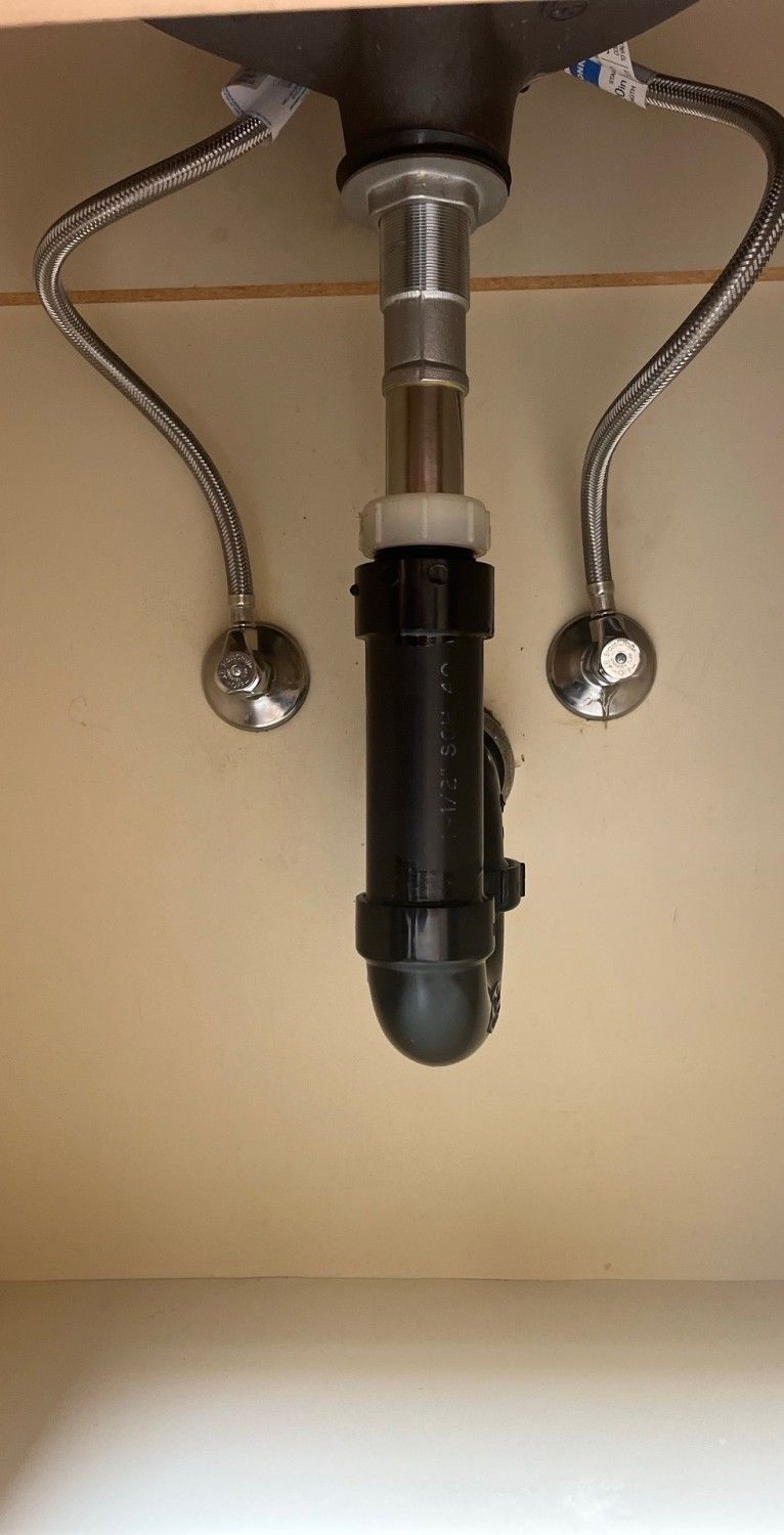 Under-sink plumbing with chrome drain pipes and a black P-trap beneath a sink