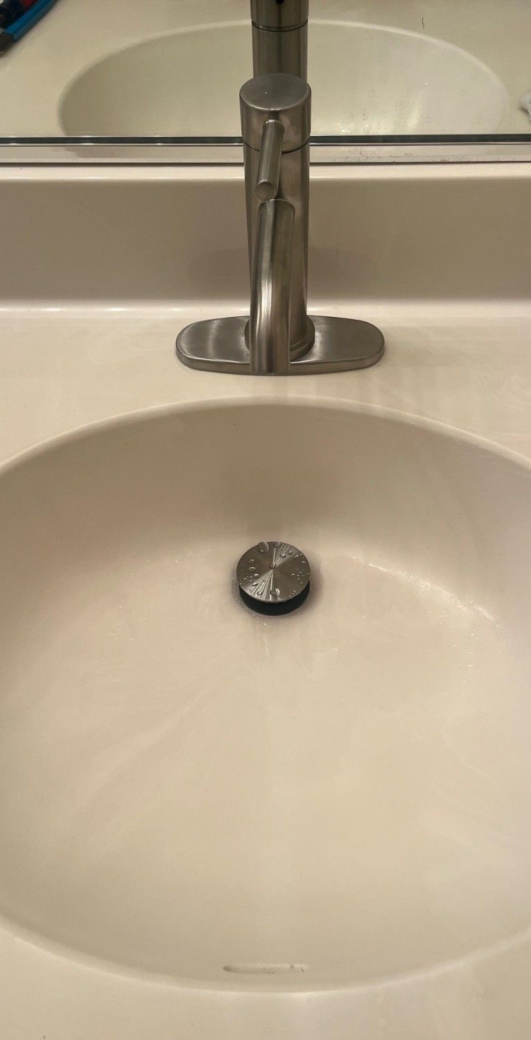 Bathroom sink with chrome faucet and white basin, showing a drain stopper in the center.
