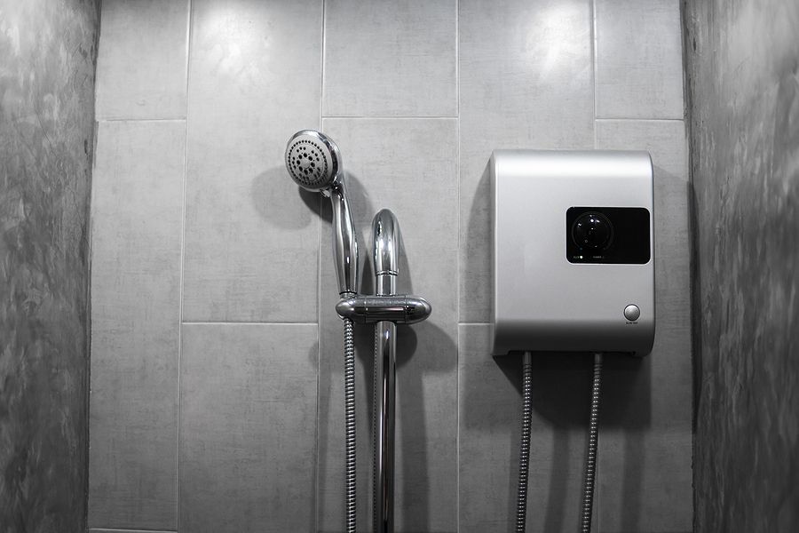 Gray tiled restroom wall with a showerhead, hose, and wall-mounted soap dispenser