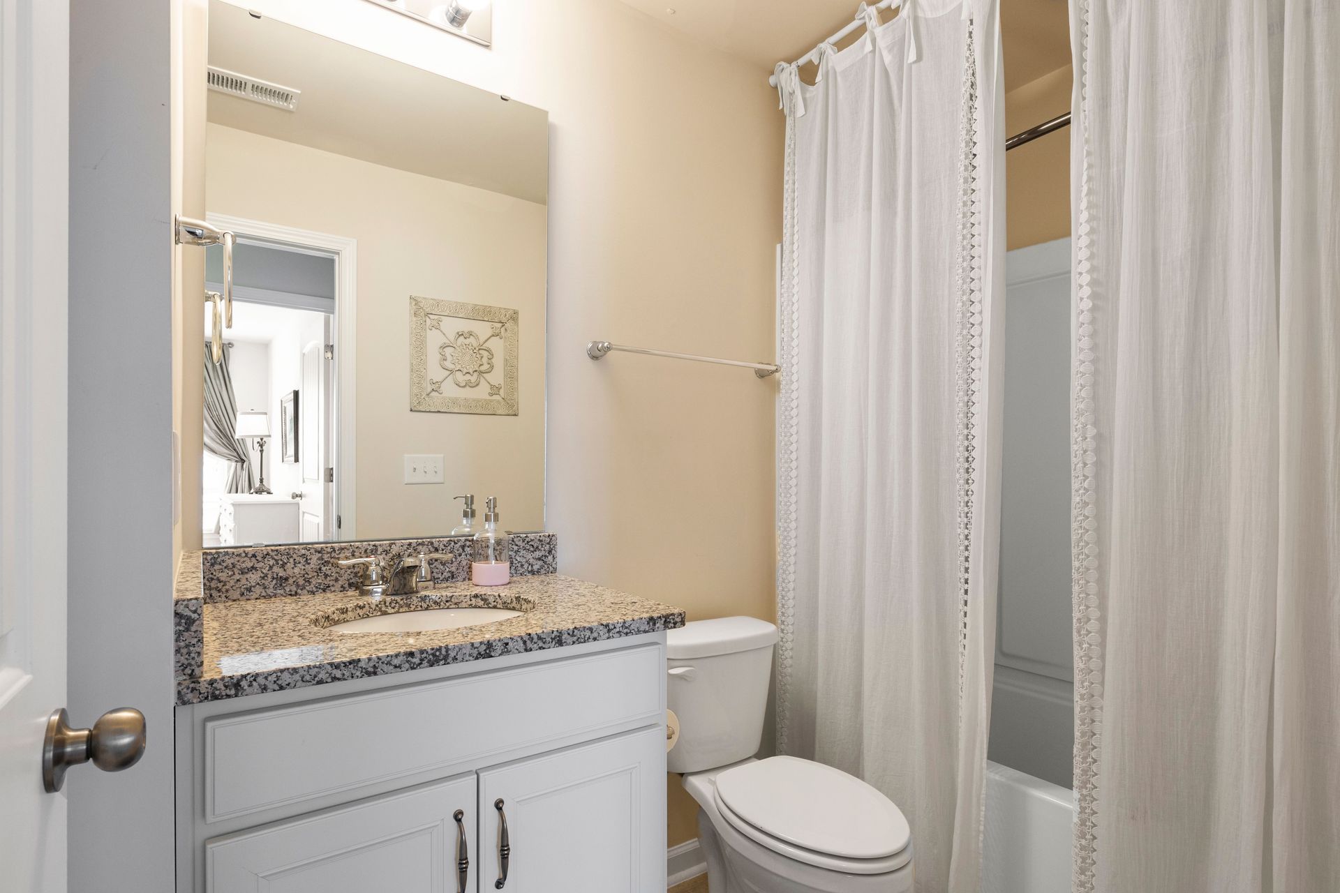 Small bathroom with granite vanity, toilet, mirror, and white shower curtain.