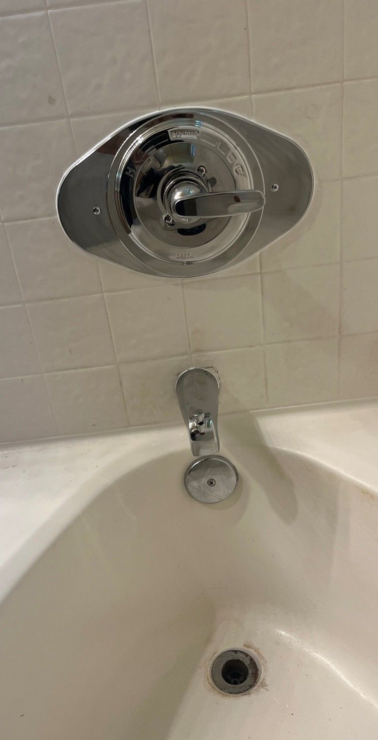 Bathtub with chrome shower control and faucet against white tiled wall.