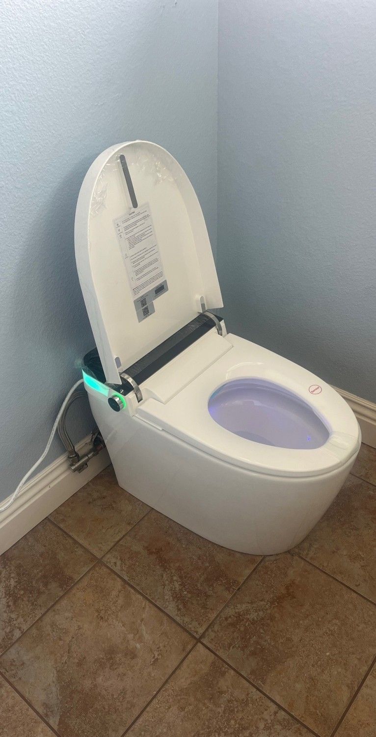 White toilet with lid up in a corner bathroom, against light gray walls and tan tile floor.
