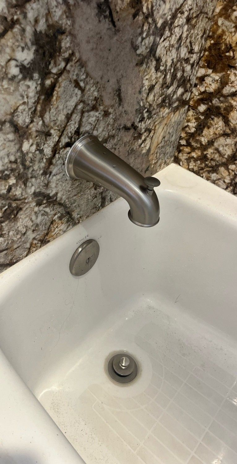 Stainless steel faucet over white sink with a marbled stone backsplash