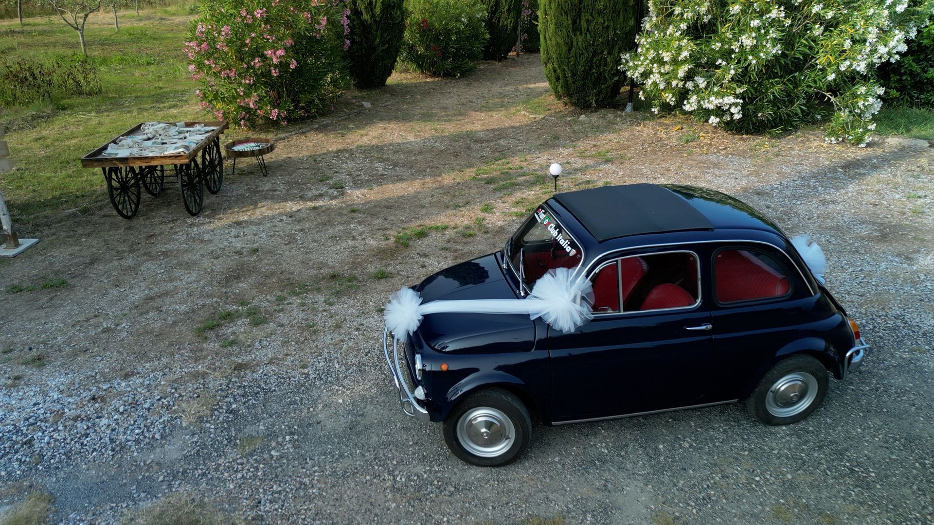 Macchinina giocattolo d'epoca blu scuro con interni rossi parcheggiata sulla ghiaia accanto a un tavolino in giardino.