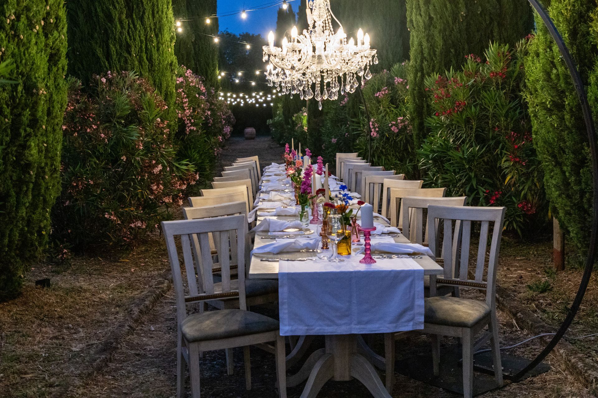 Elegante tavolo da pranzo all'aperto, posizionato sotto lampadari lungo un sentiero del giardino