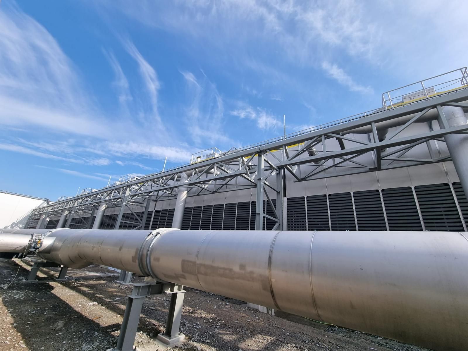 Large industrial cooling tower with metal piping against a blue sky.