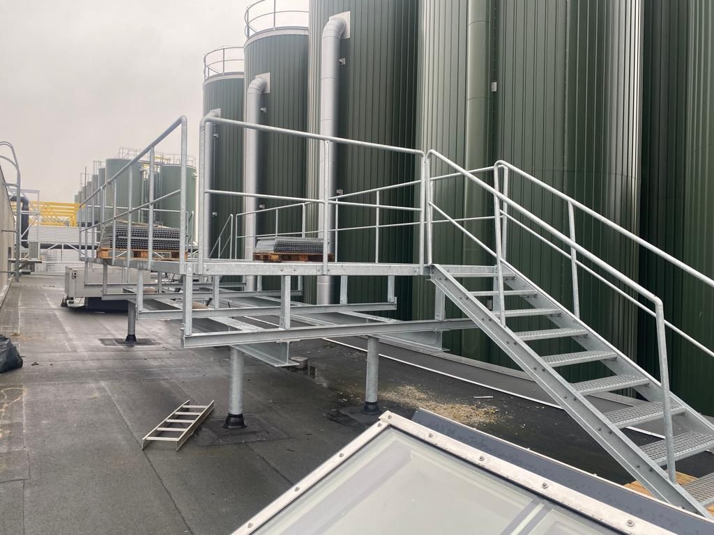 Metal platform and stairs next to large green industrial tanks on a flat roof.