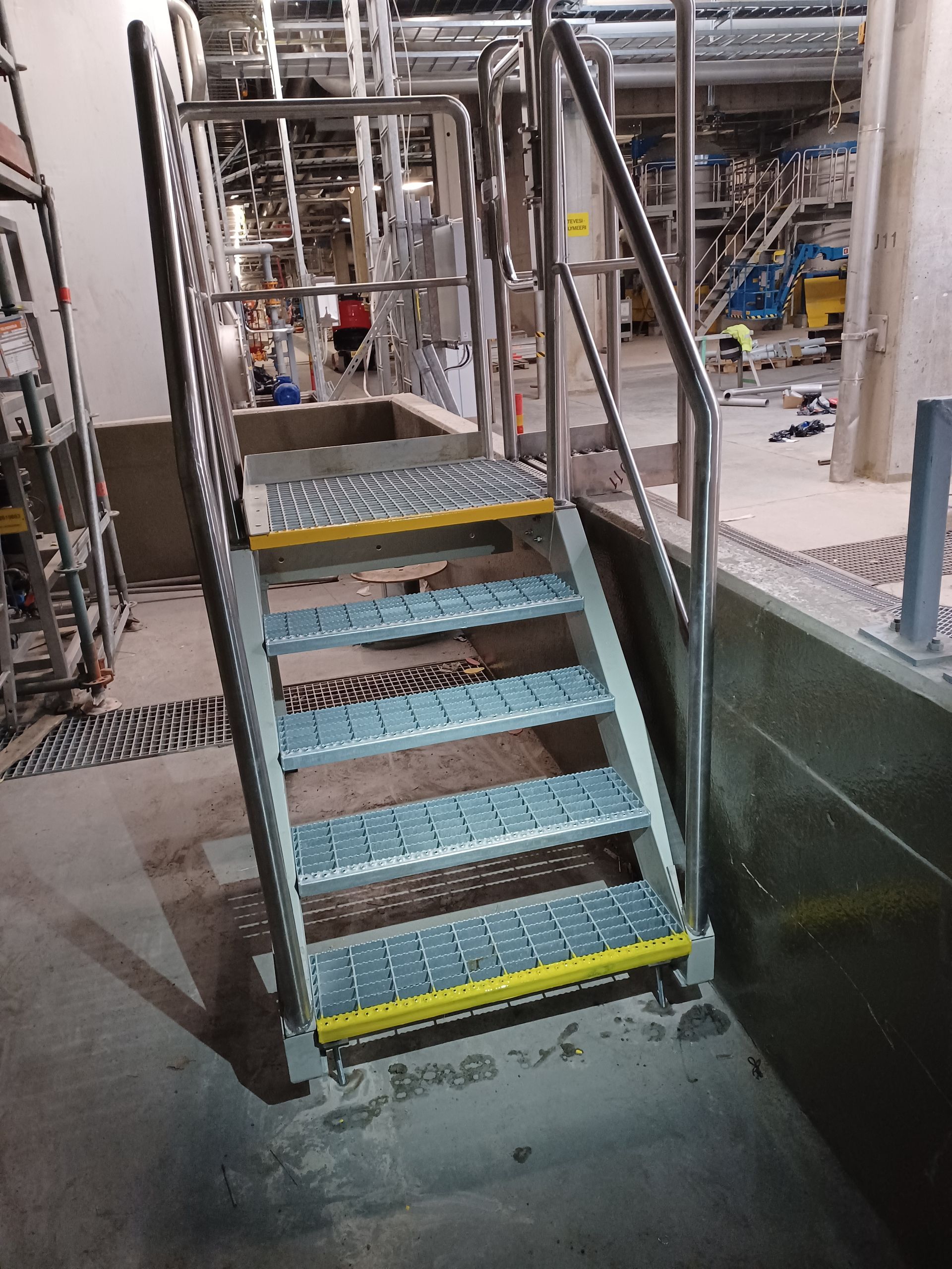 Metal staircase with yellow edges and handrails in a factory setting.