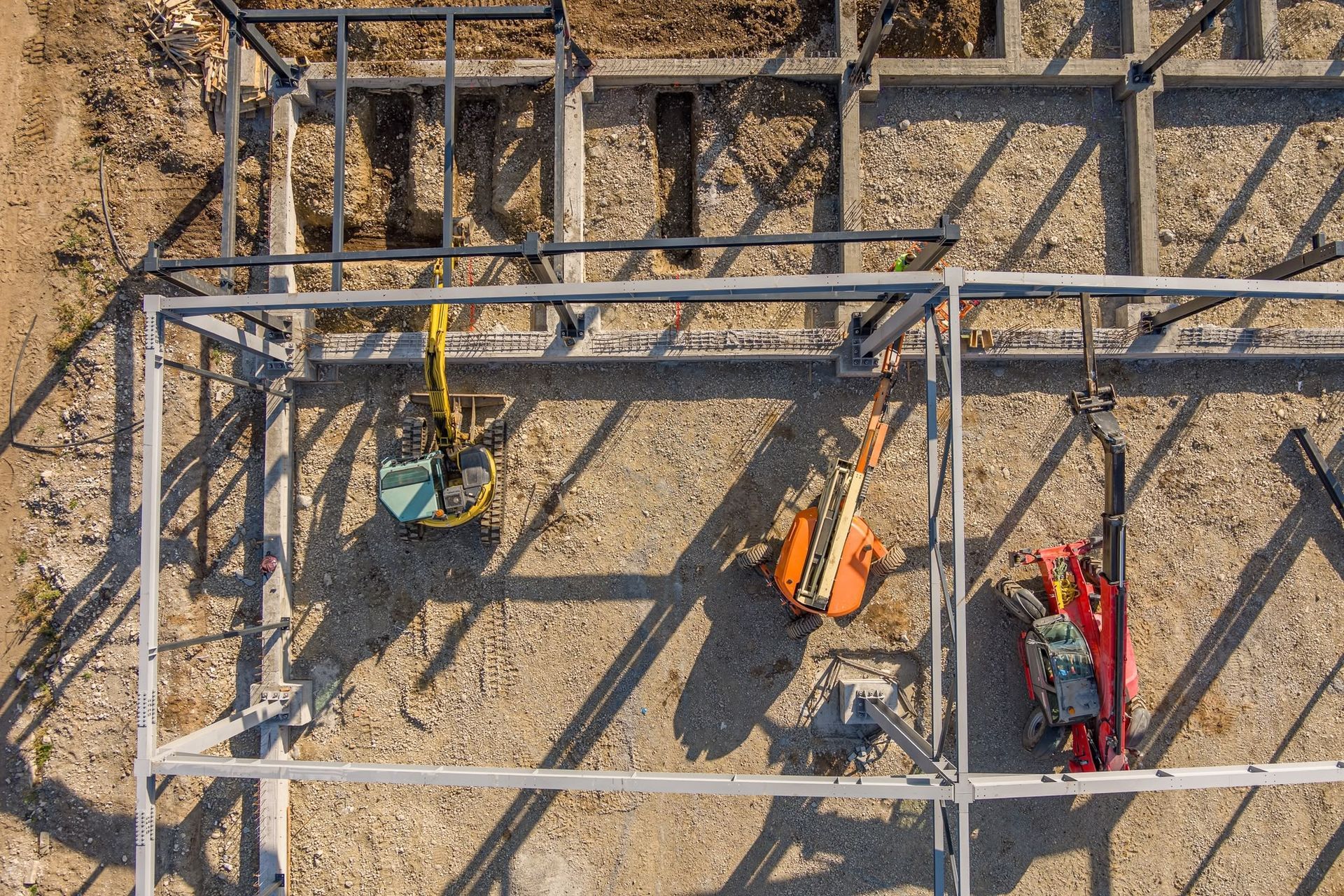 Overhead shot of a construction site with three pieces of machinery inside metal frame structures.