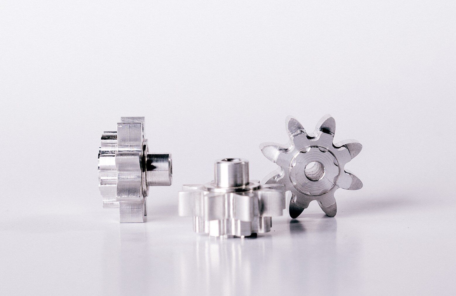 Three small, shiny metal gears with circular hubs, on a white surface.