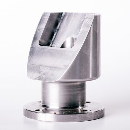 Silver metal industrial part with angled top, cylindrical body, and base with mounting holes.