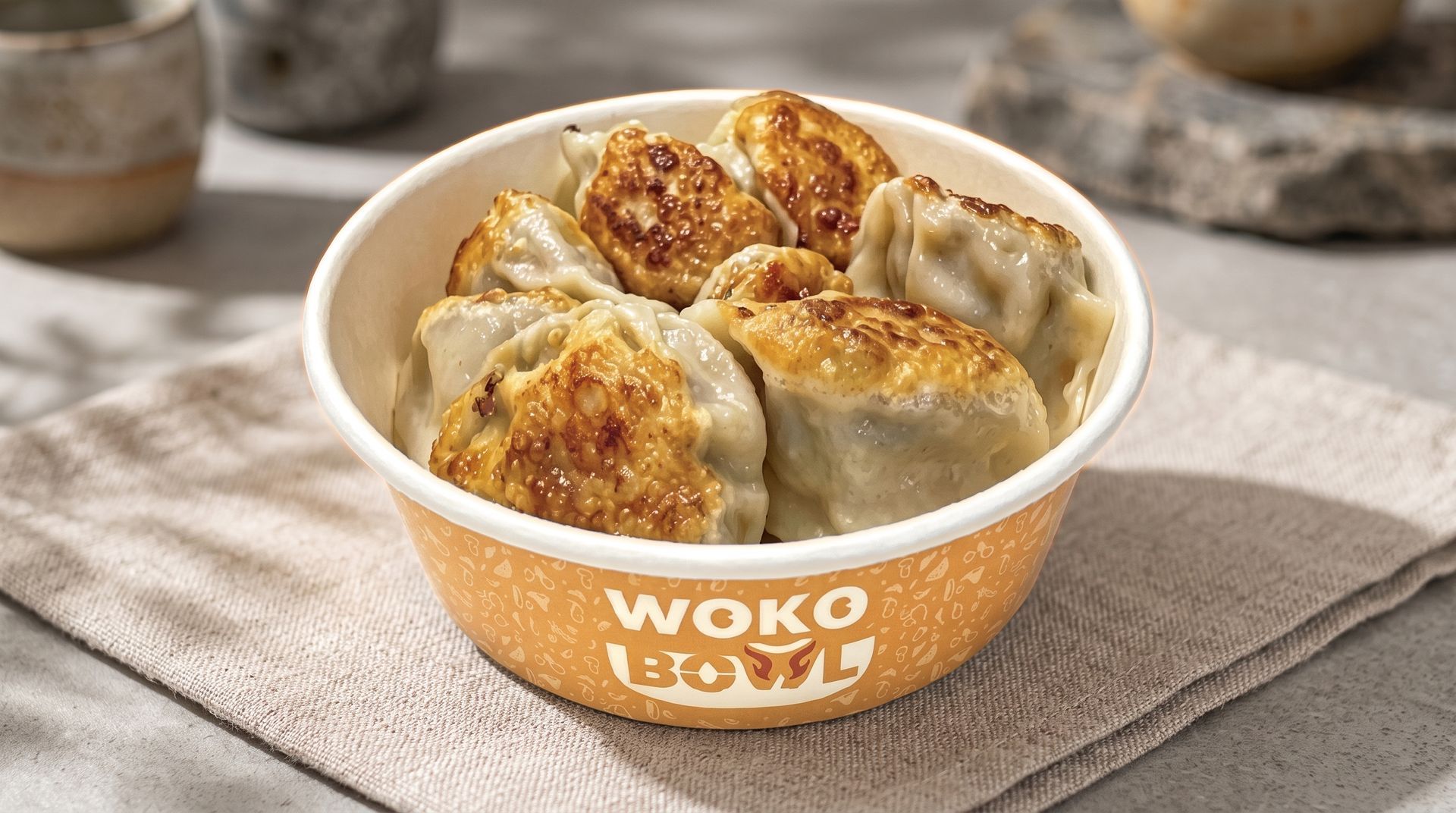 WOKO bowl of dumplings on a napkin, with browned tops and steam-like warmth on a table