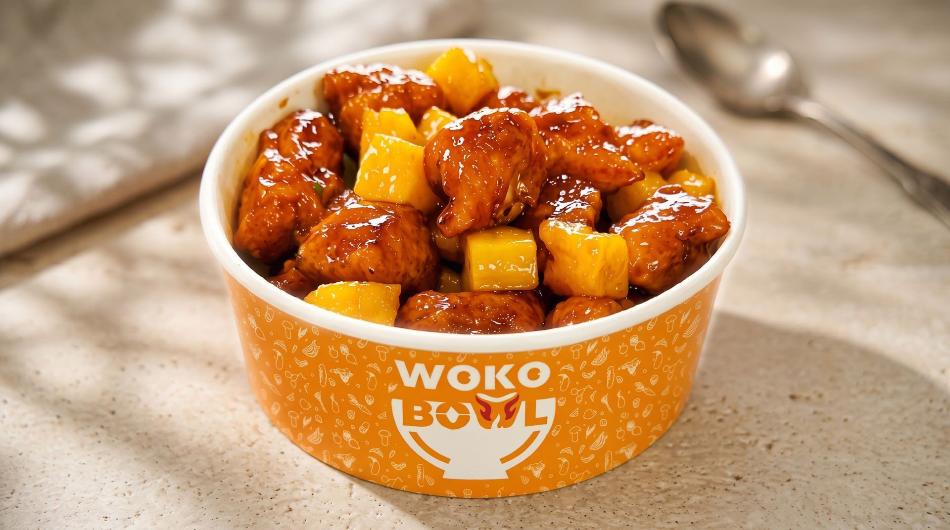 Orange takeout bowl of sweet and sour chicken with pineapple on a beige table