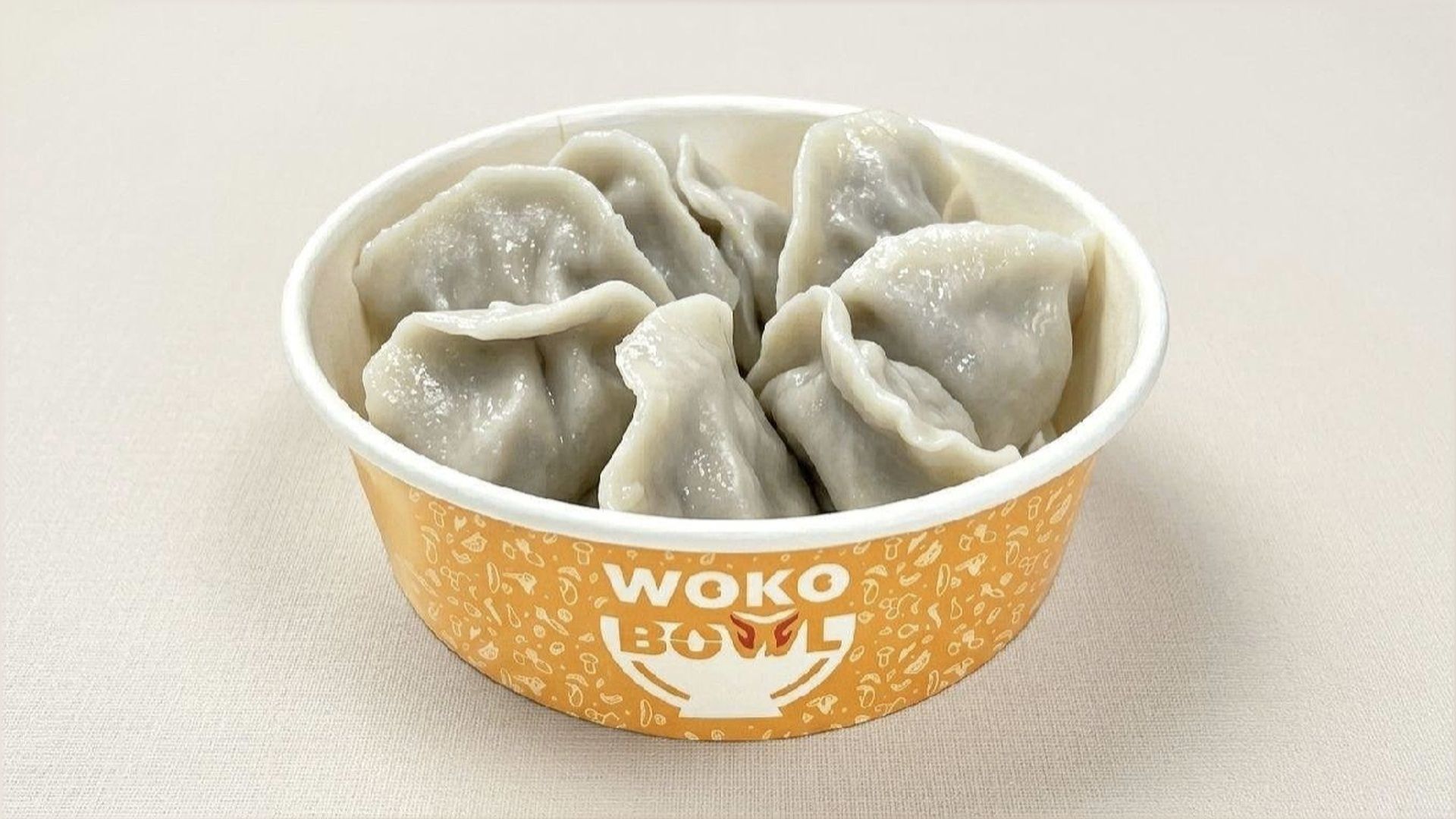 White dumplings in an orange WOKO bowl on a light background