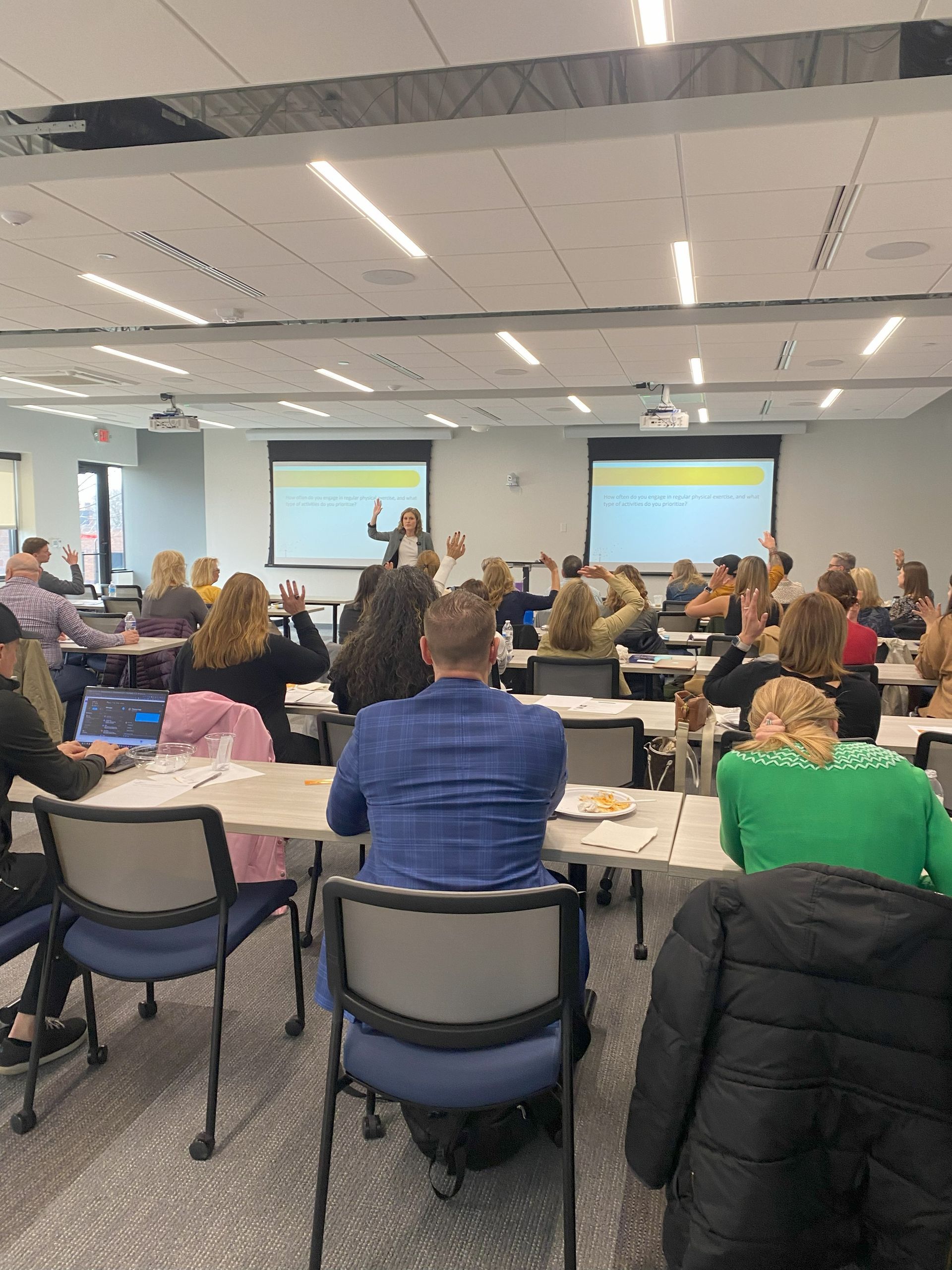 Conference audience seated in a meeting room facing presentation screens and speakers
