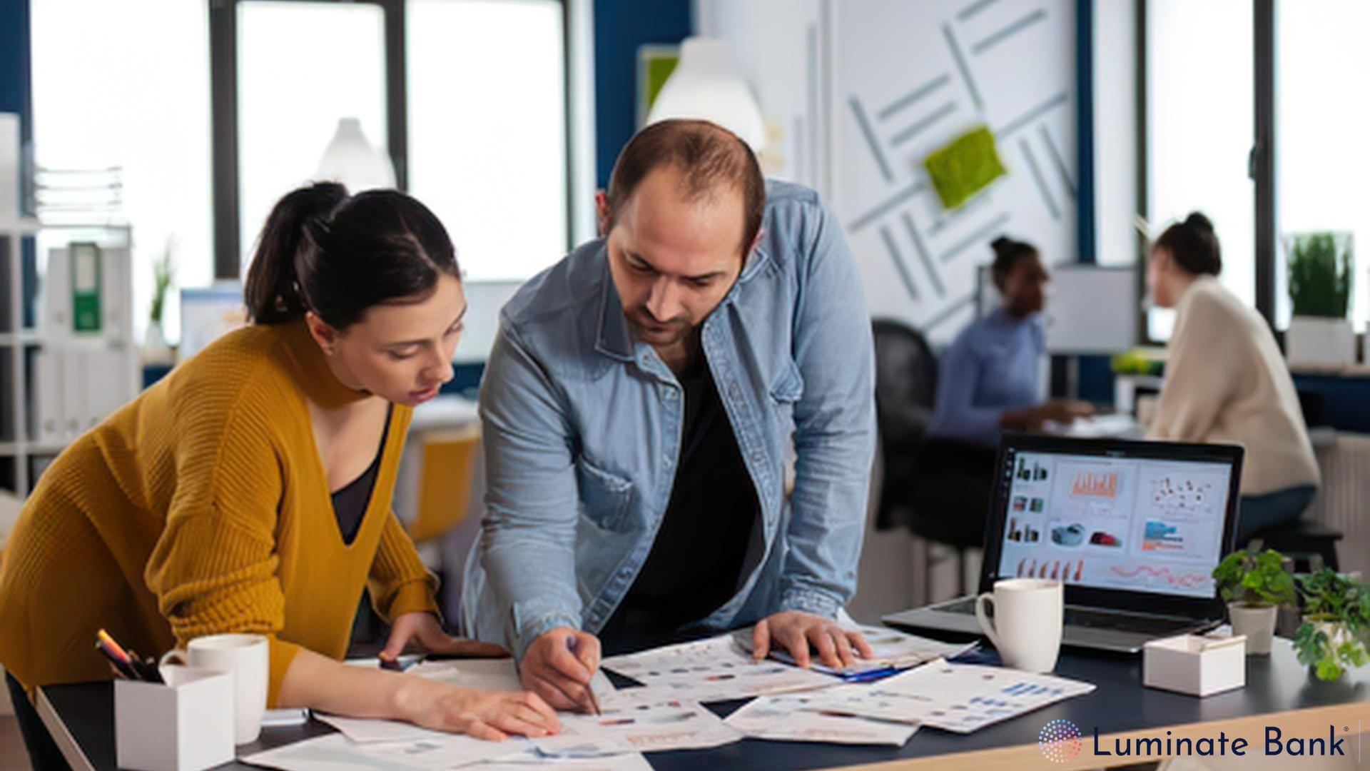Two colleagues leaning over a desk reviewing printed charts together in a bright, open office.