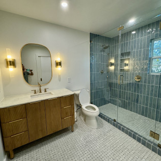 Modern bathroom with wood vanity, oval mirror, and blue tiled walk-in shower.