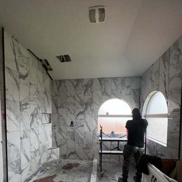 Person working in an unfinished room with marble-patterned walls and arched windows.
