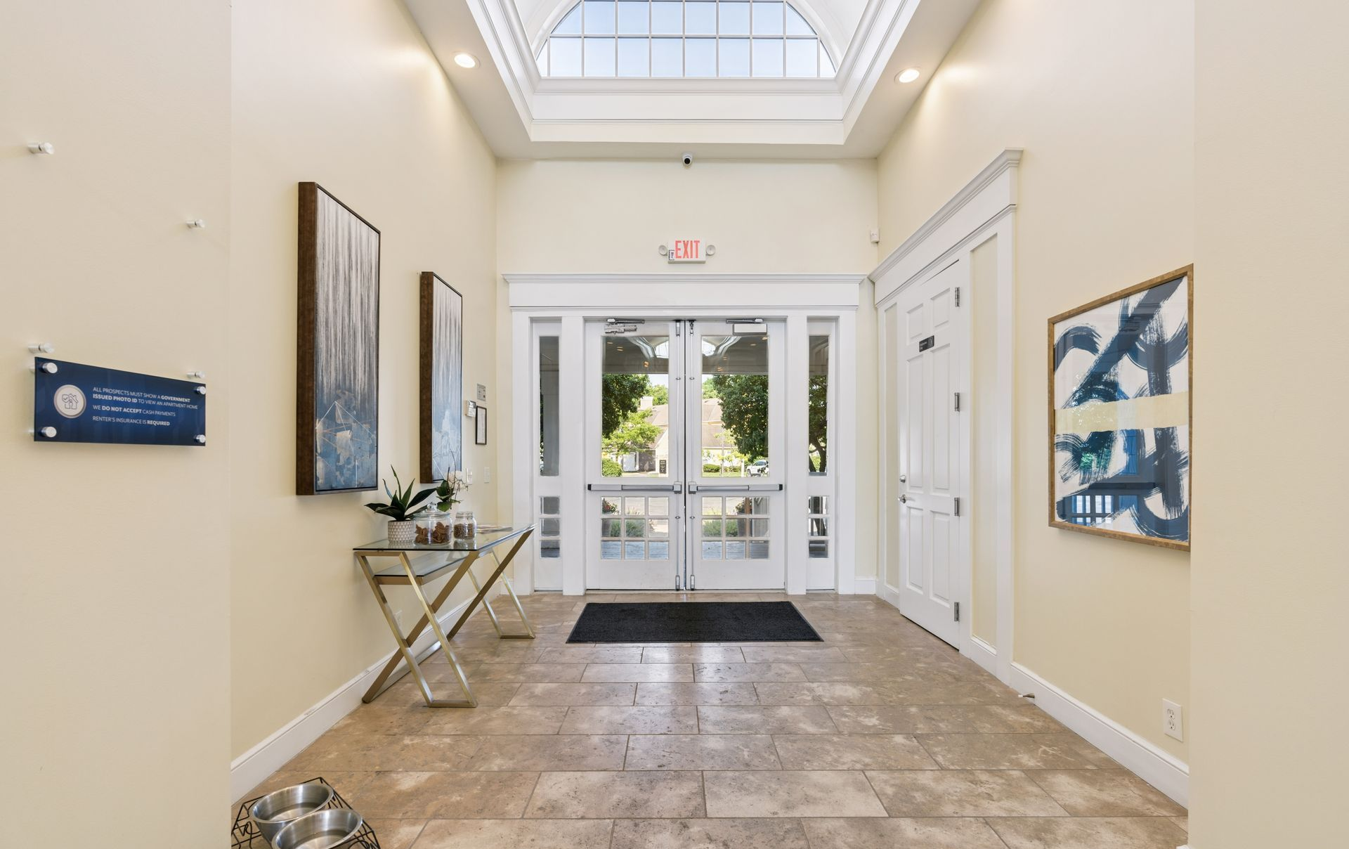 Bright office lobby with glass doors, skylight, tiled floor, and wall art.