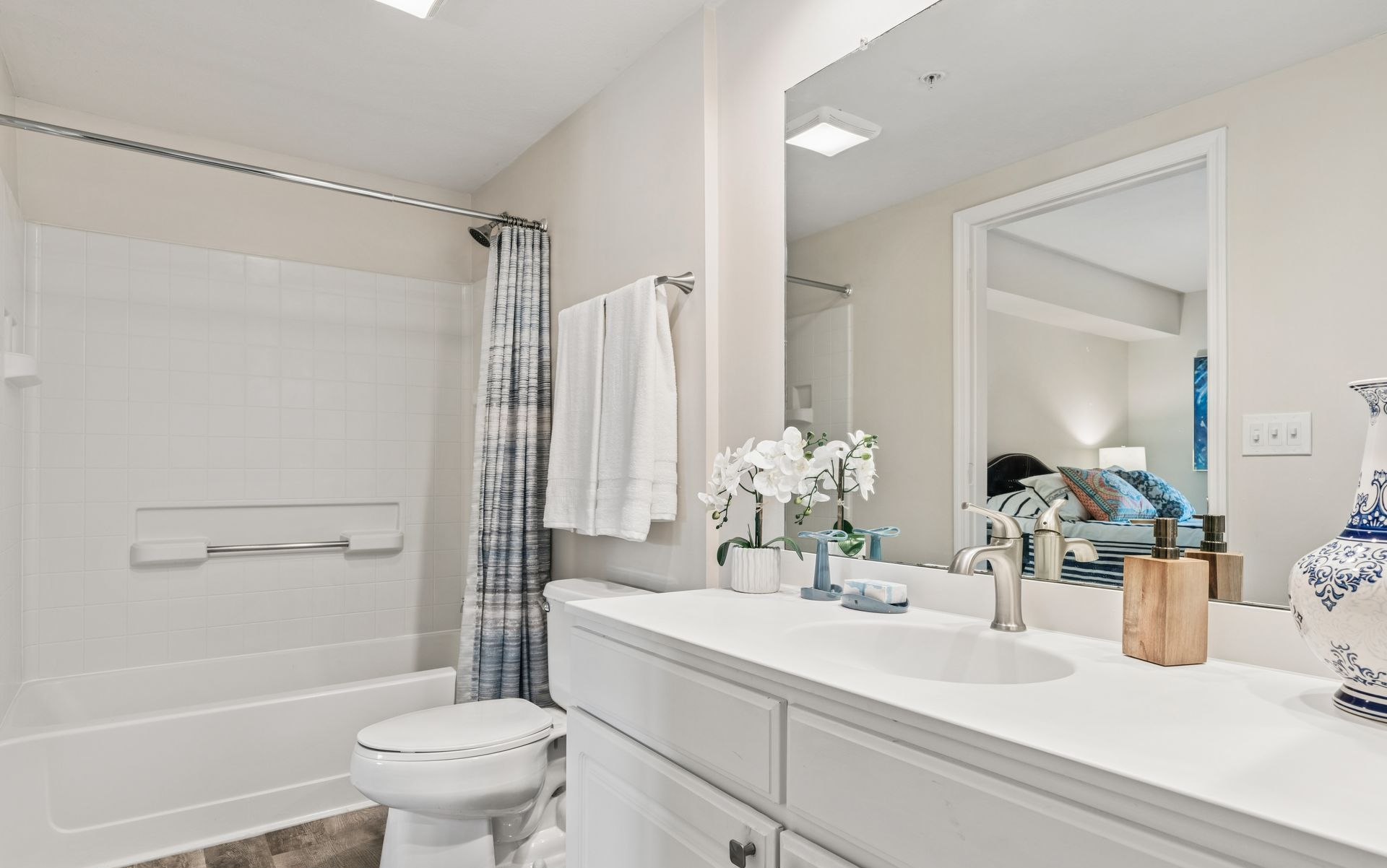 Bright bathroom with white vanity, mirror, bathtub, toilet, and blue shower curtain.