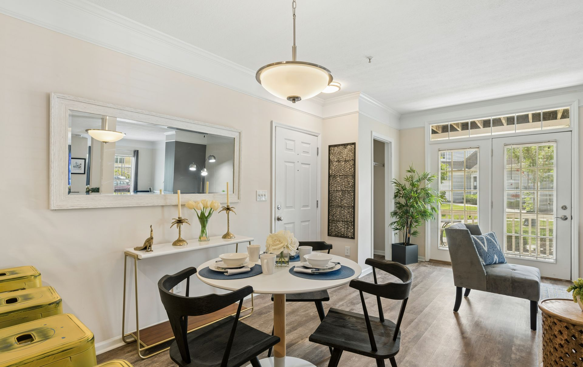 Bright dining room with round table, black chairs, mirror, sideboard, and large windows by the patio.