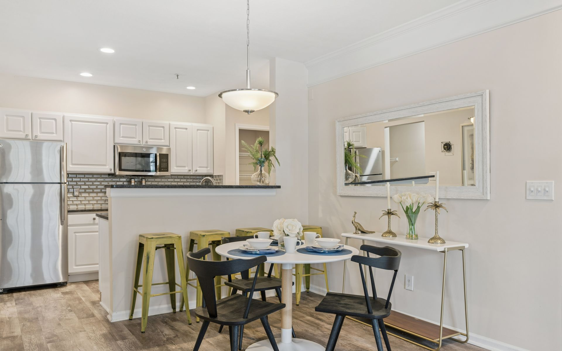 Bright kitchen with white cabinets, stainless appliances, a round dining table, and a mirrored wall accent.