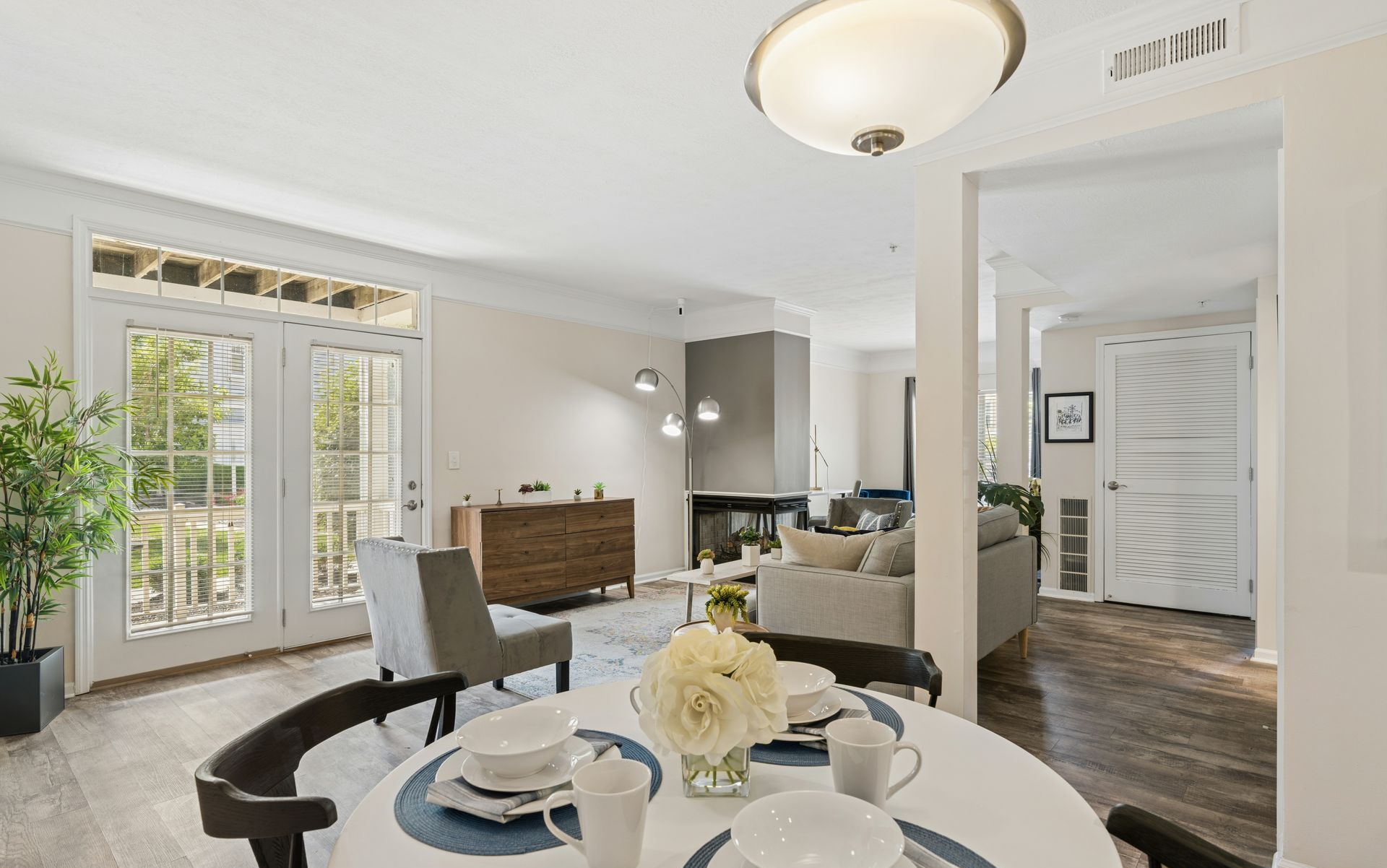 Bright dining and living room with white chairs, dark table, French doors, and wood flooring.