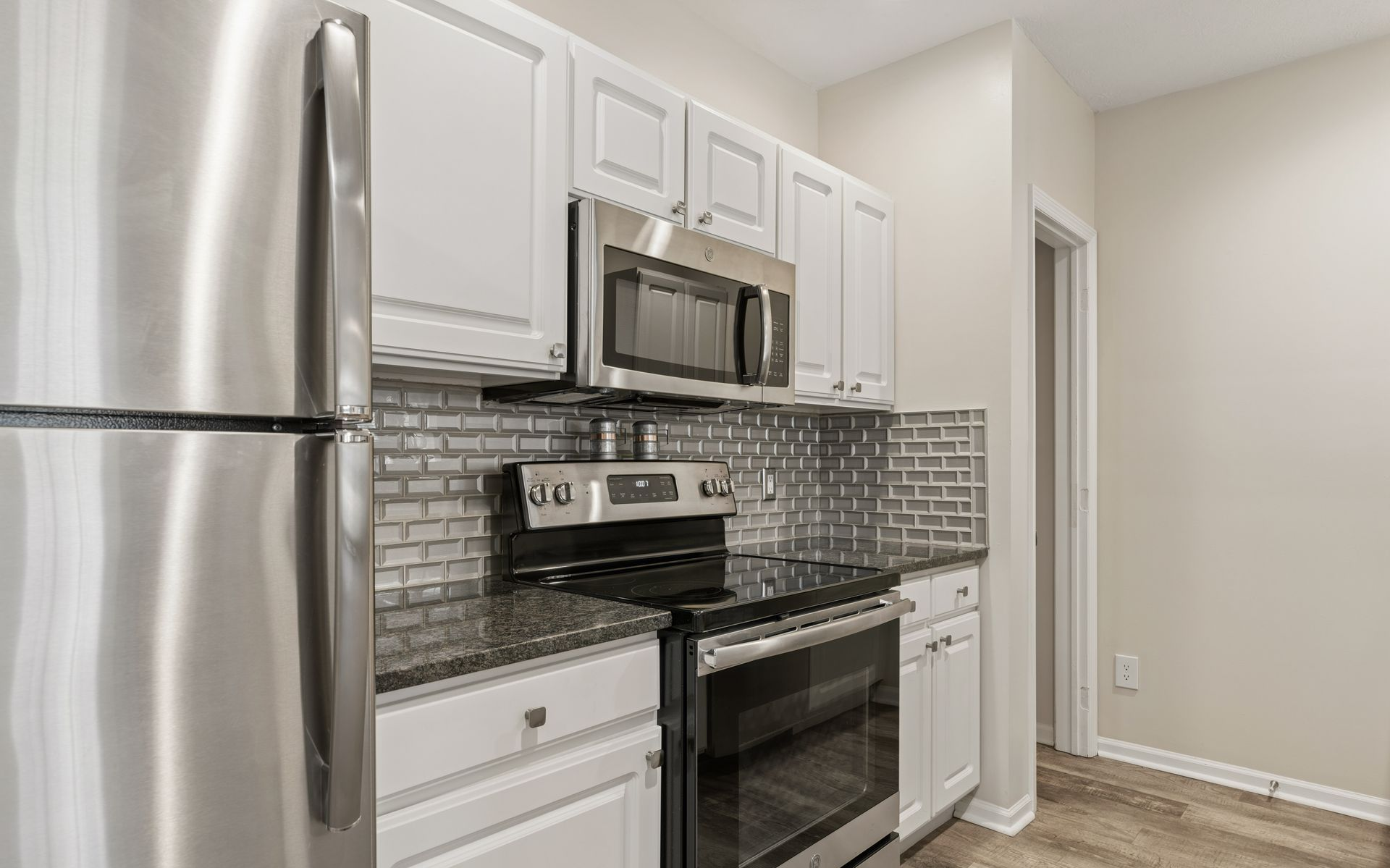 Modern kitchen with stainless steel appliances, white cabinets, mosaic backsplash, and wood-look flooring.