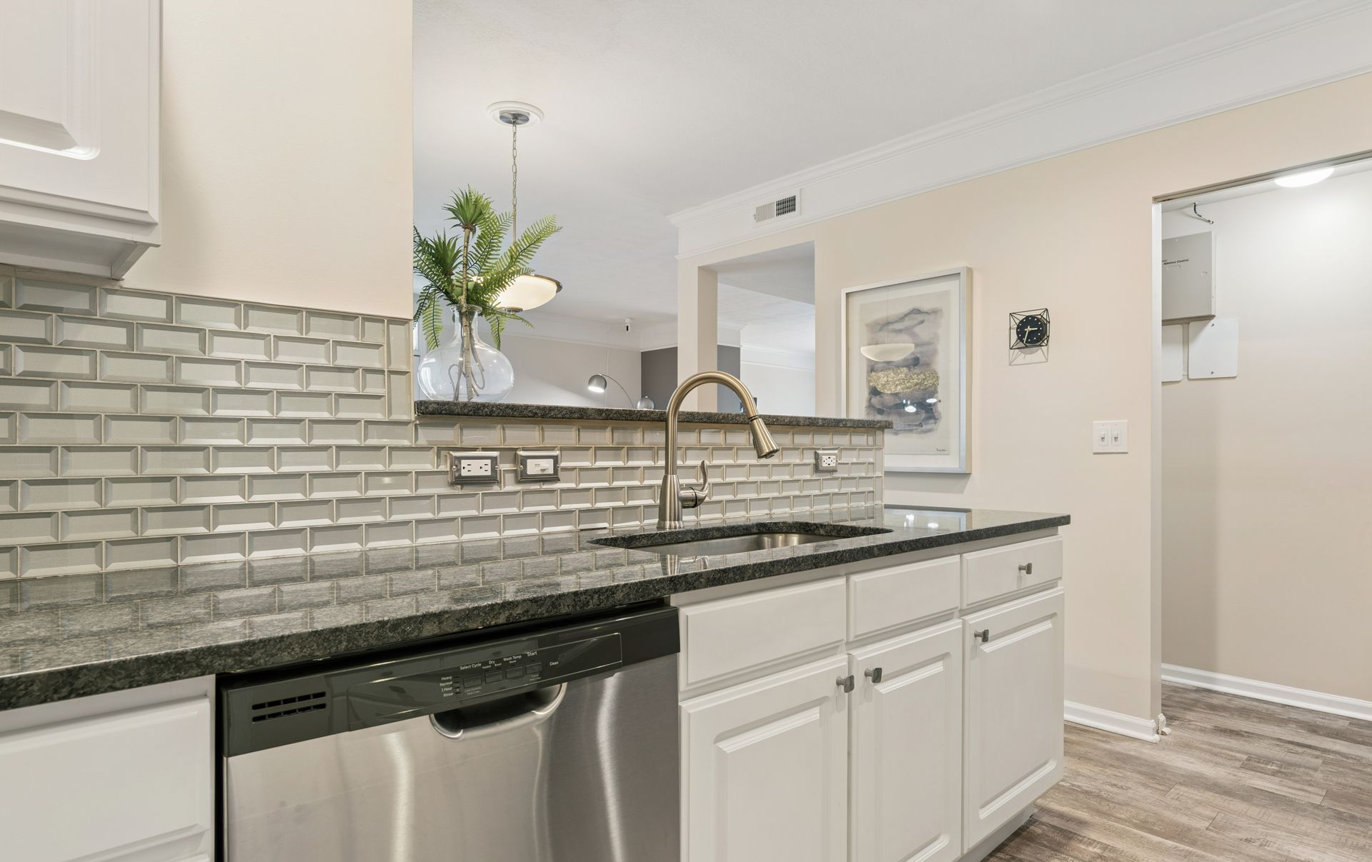 Modern kitchen with white cabinets, gray subway tile, granite countertop, stainless dishwasher, and brass faucet.