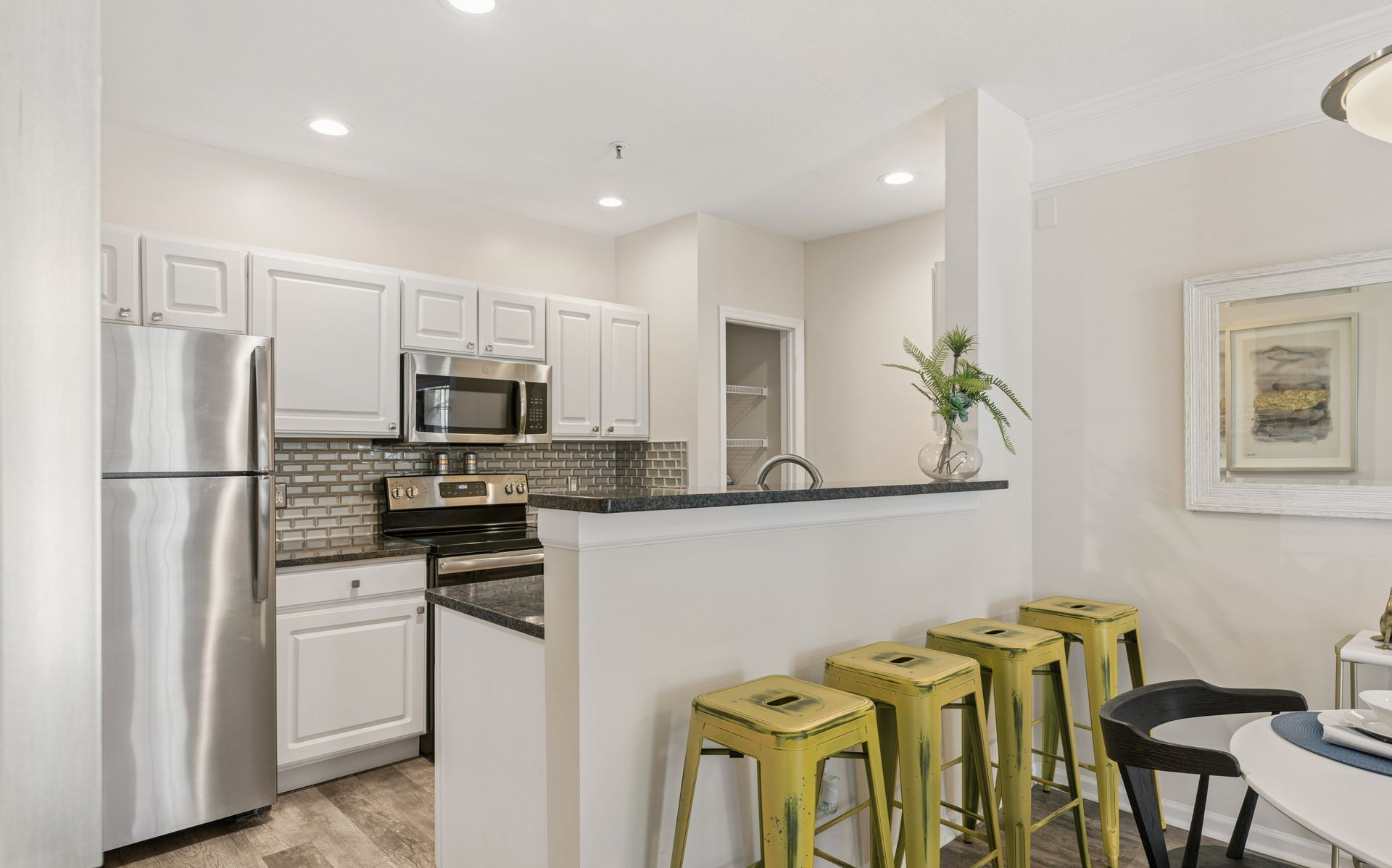 Bright modern kitchen with stainless steel appliances, white cabinets, and yellow bar stools at a breakfast counter.