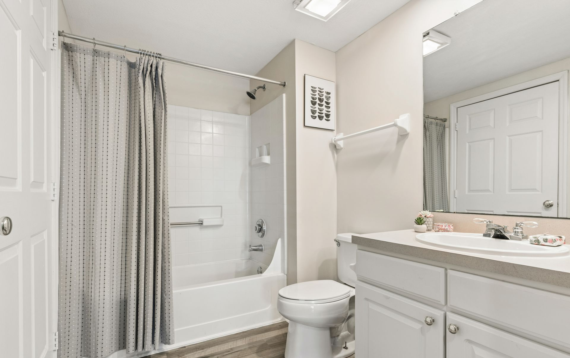Bright white bathroom with tub, shower curtain, toilet, vanity, and mirror.