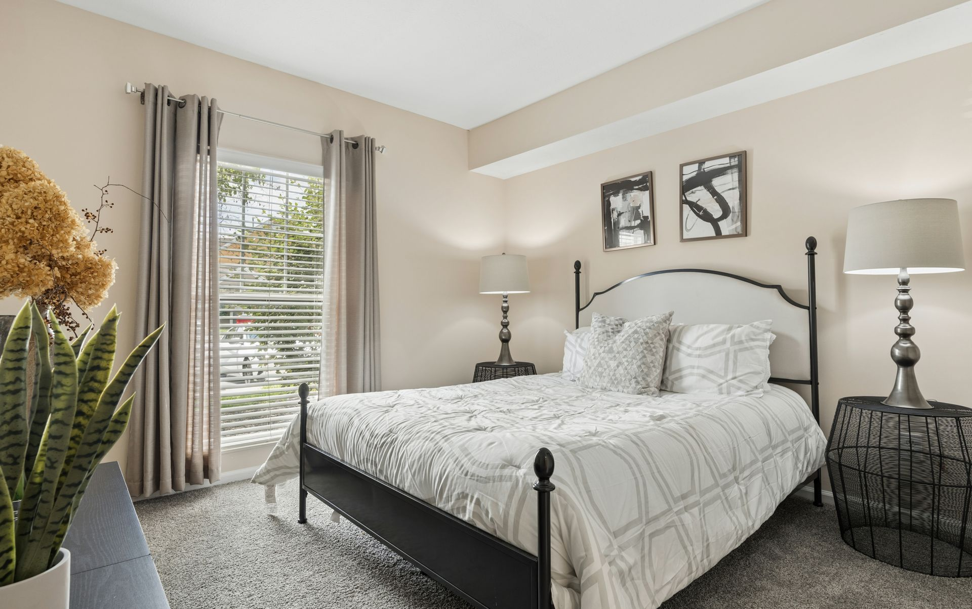Cozy bedroom with a black metal bed, gray bedding, white walls, and a window with curtains.