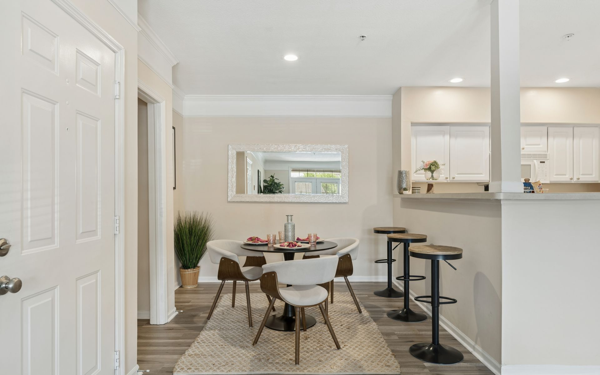 Bright dining area with table, chairs, rug, and adjacent kitchen with bar stools.
