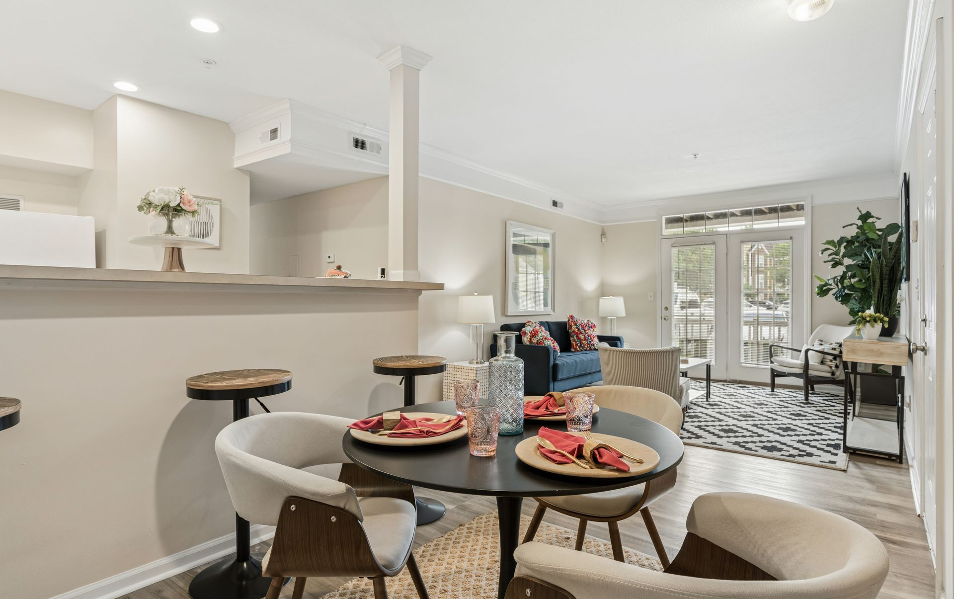 Modern open-plan dining and living room with round table, beige chairs, and large windows.