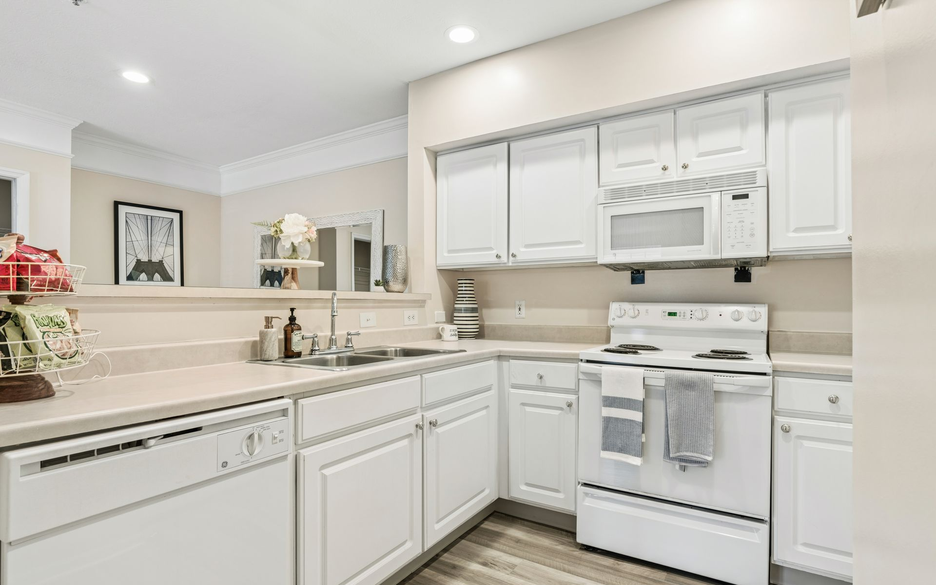 Bright white U-shaped kitchen with stove, dishwasher, cabinets, and beige countertops.